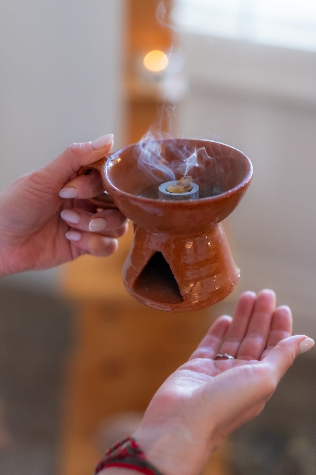Two hands holding a smoking terracotta incense burner during a ceremonial healing