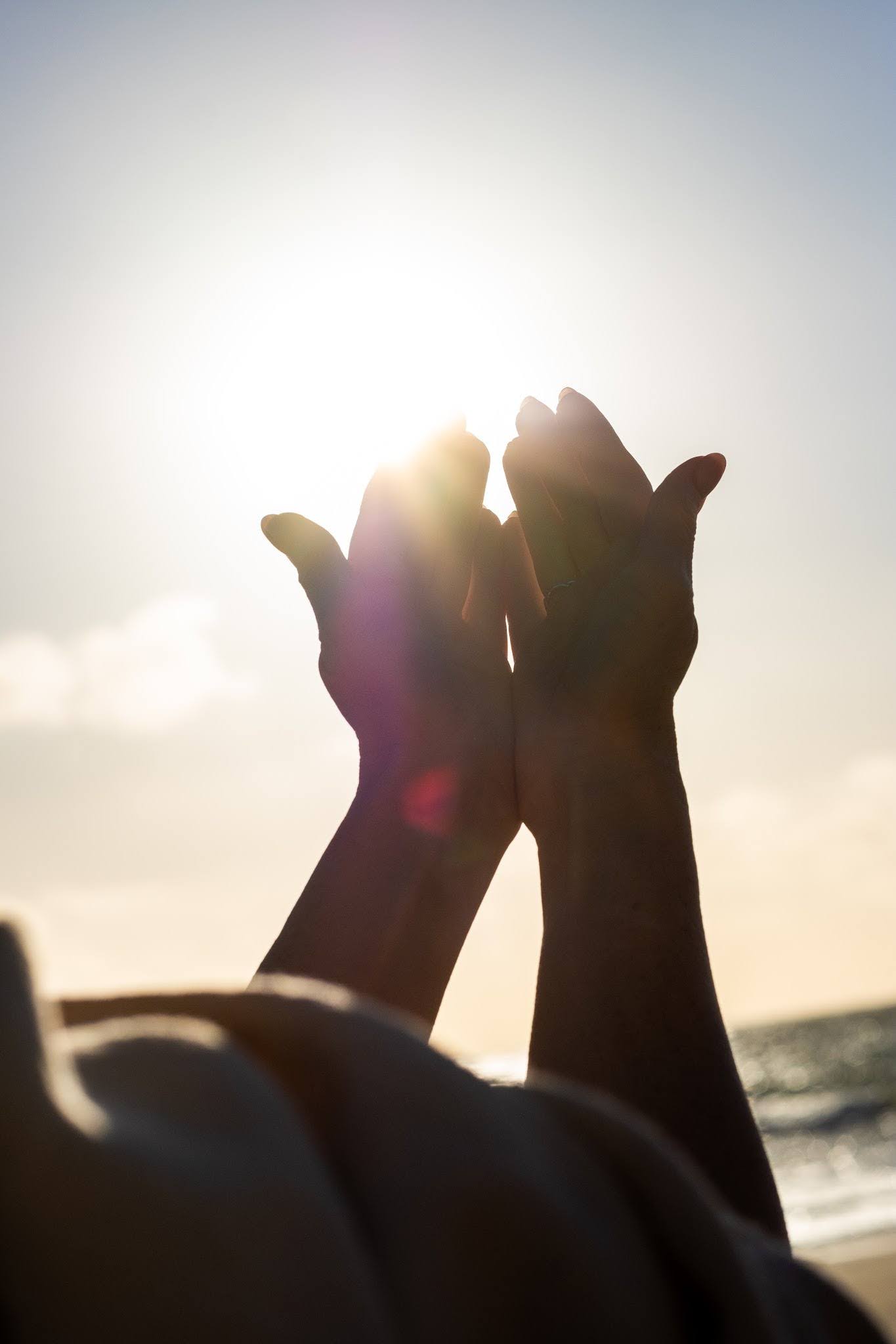 Hands lifted toward sunlight over the ocean