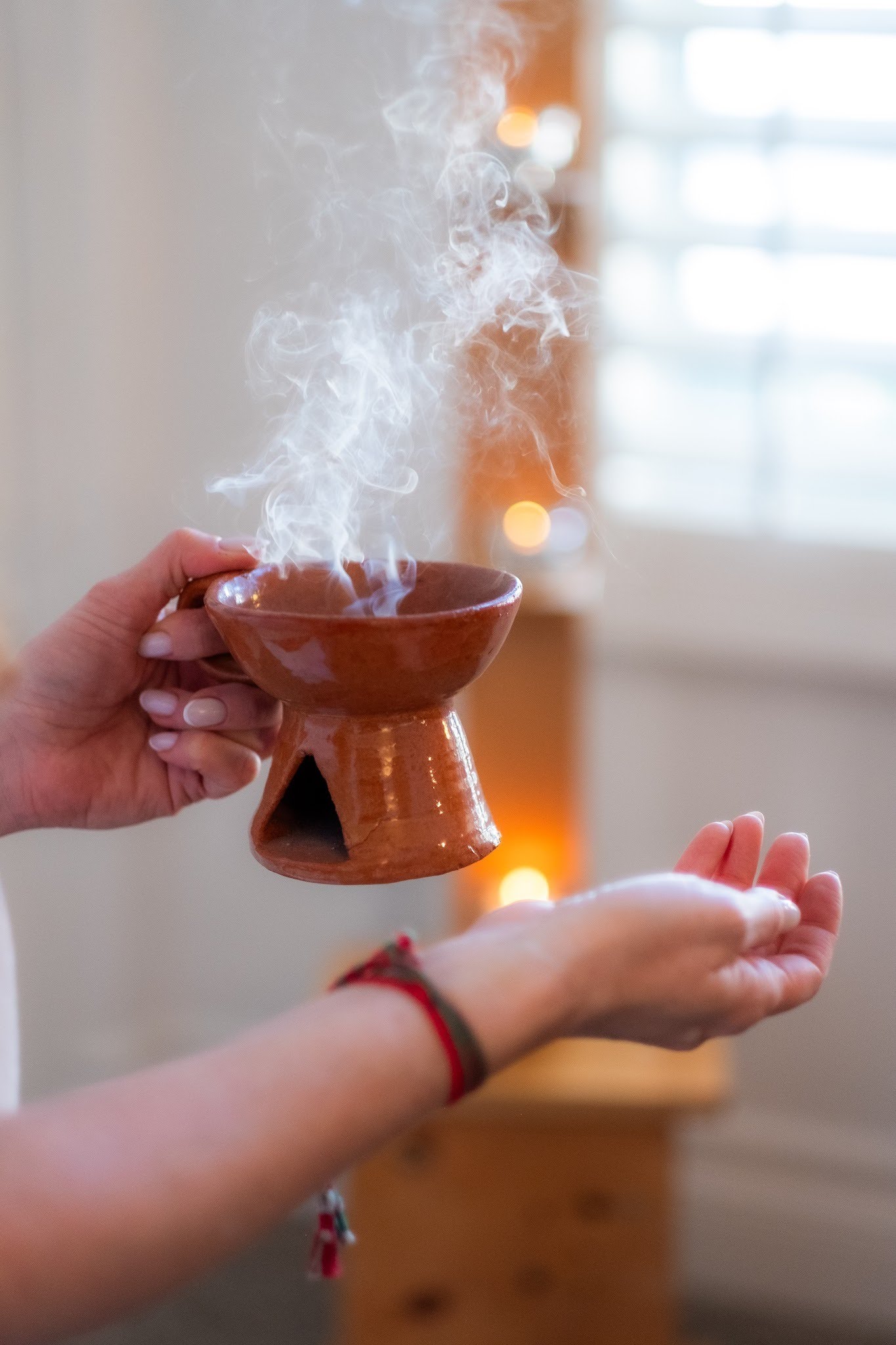 Two hands holding a smoking terracotta incense burner during a home clearing ceremony