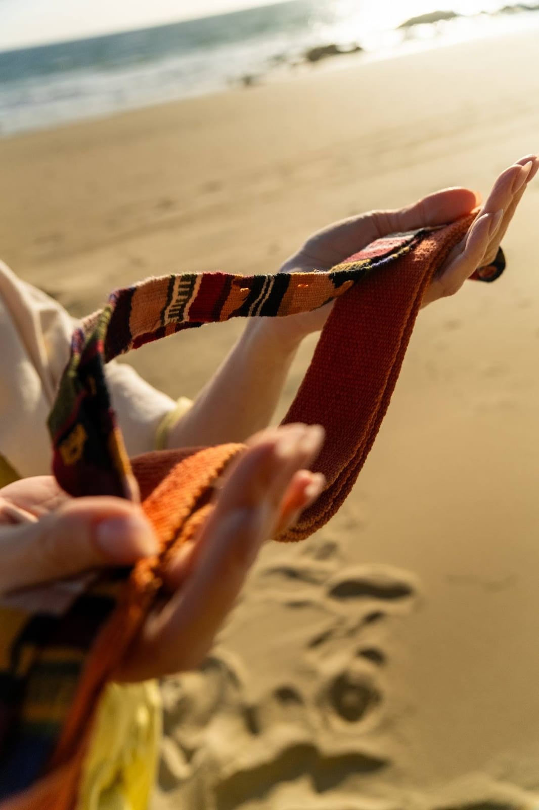 Two hands holding a woven textile on a sunlit beach — relationship healing session