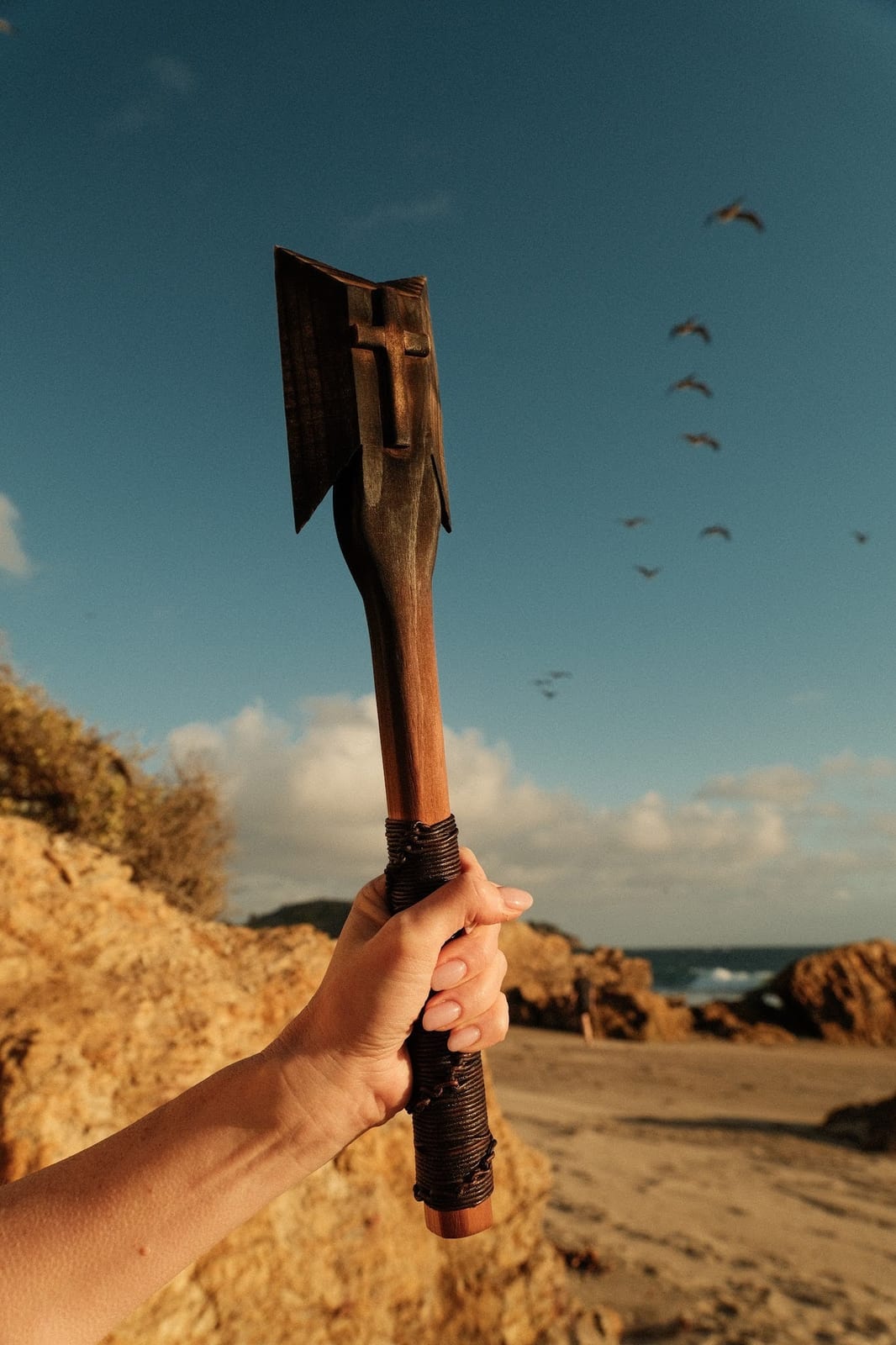 A carved wooden ritual blade held against a bright blue sky — used in spiritual interference and witchcraft removal