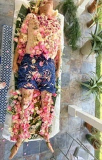 A person covered in fresh pink roses, herbs, and flowers during a traditional shamanic healing ceremony